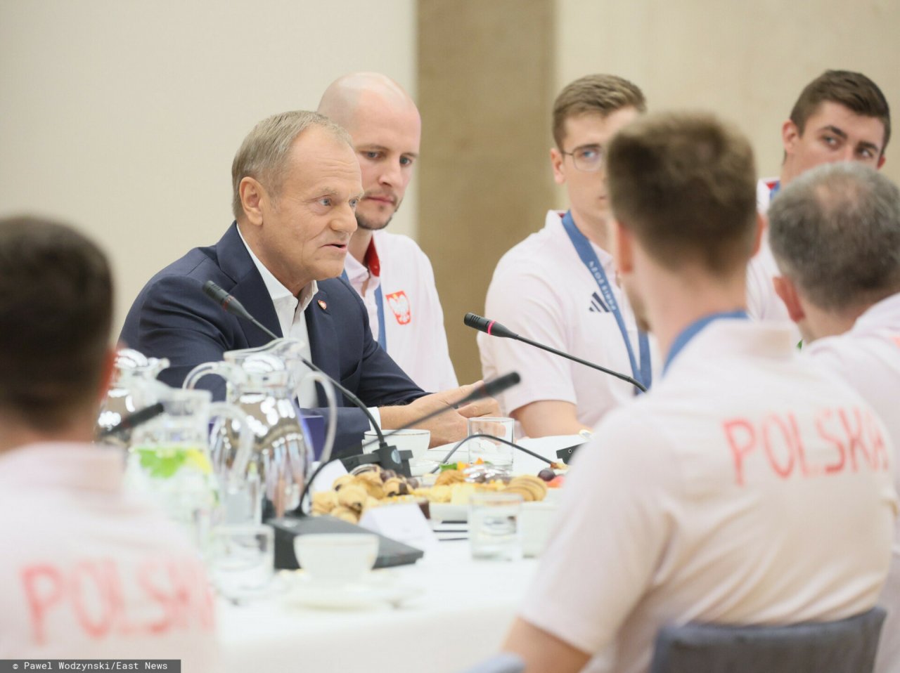 Donald Tusk w garniturze obok sportowców ubranych na biało