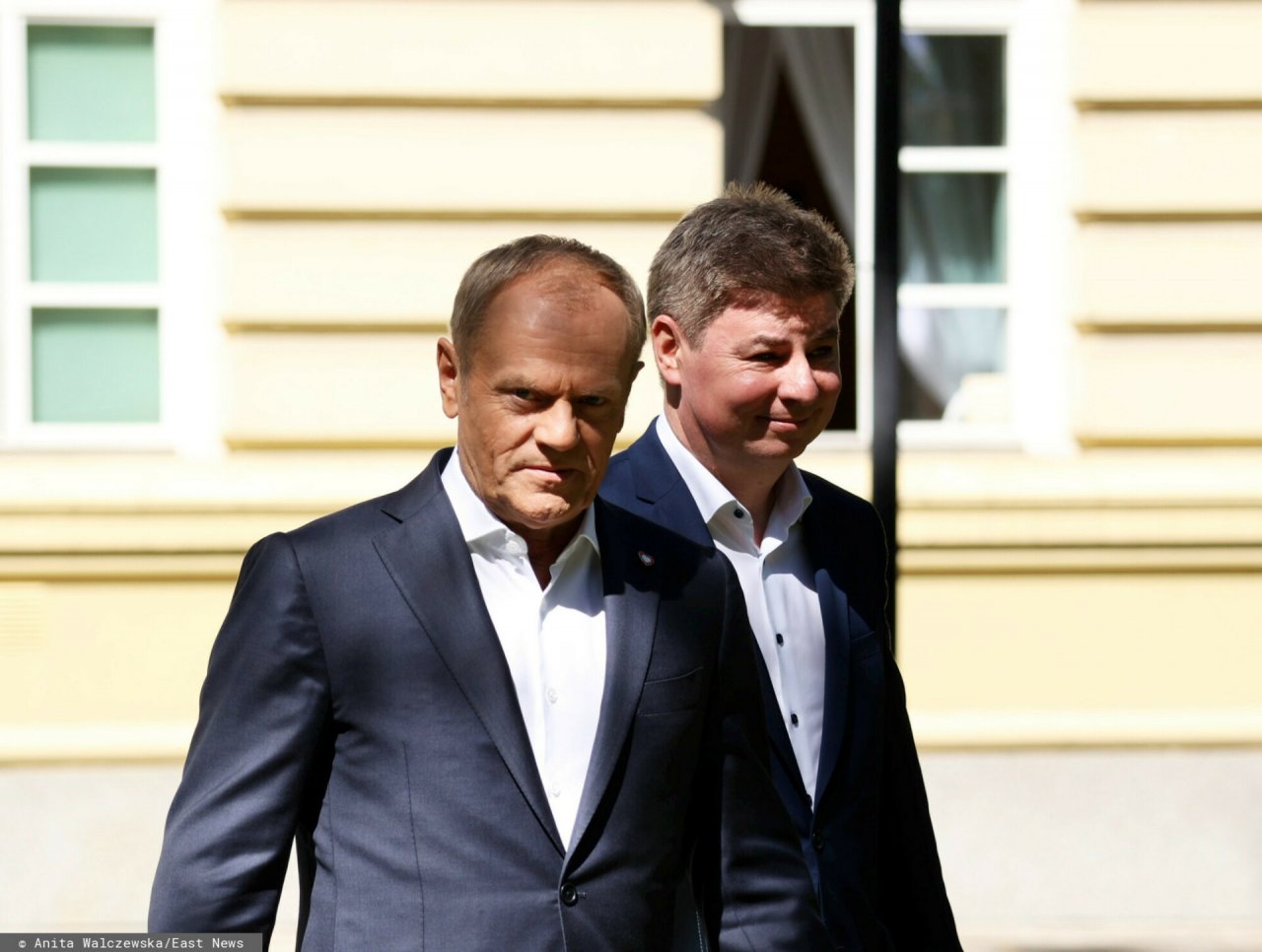 Donald Tusk w garniturze a za nim Jan Grabiec w garniturze