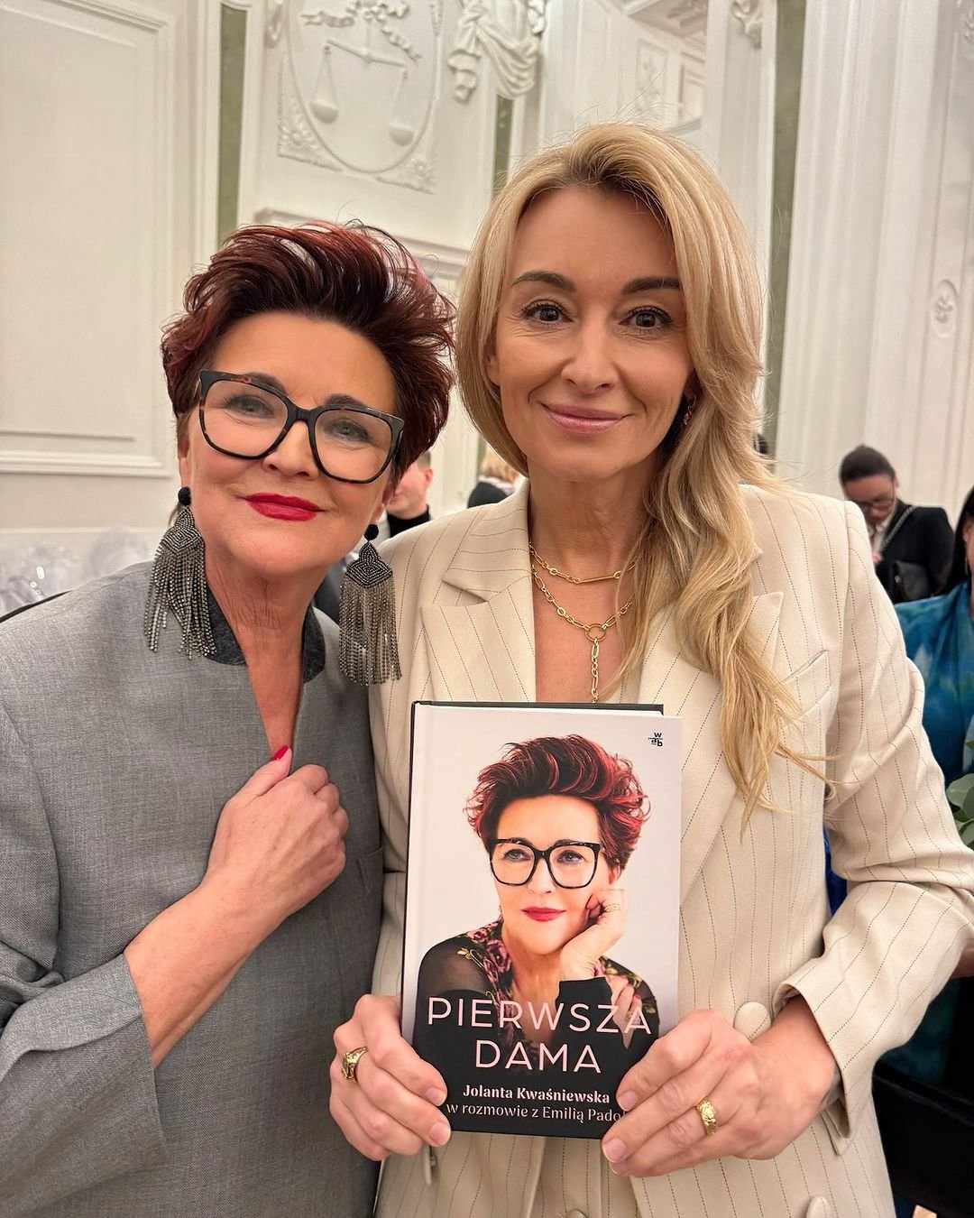 Jolanta Kwaśniewska w okularach i dużych kolczykach oraz Martyna Wojciechowska w beżowym żakiecie, z książką Pierwsza dama