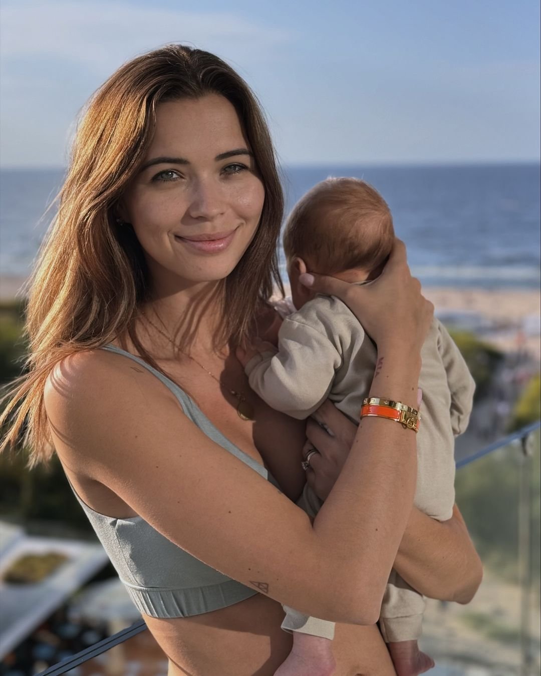 Sandra Kubicka w letnim topie z dzidziusiem na rękach, na tle morza