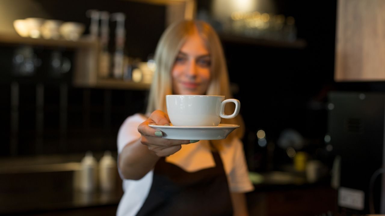 Młoda kobieta jako baristka w kawiarni podaje kawę