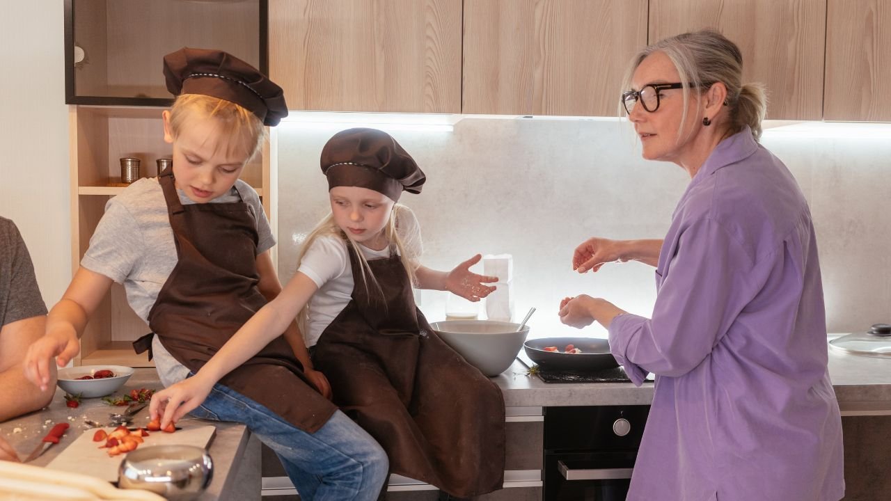 Babcia gotuje w kuchni z dwoma wnuczkami w kucharskich strojach