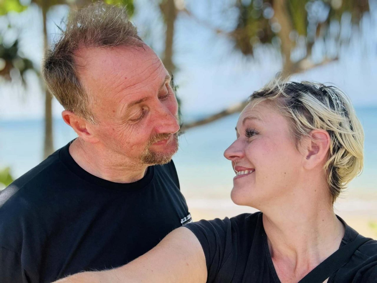 Vince i Dominika Clarke w czarnych koszulkach spoglądają na siebie na tajskiej plaży