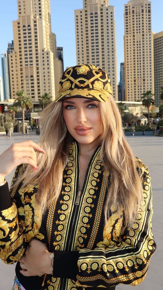 Caroline Derpieński we wzorzystej, złoto-czarnej bomberce i czapce na tle dubajskich wieżowców