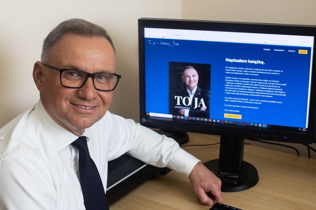 Andrzej Duda ubrany na biało obok książki