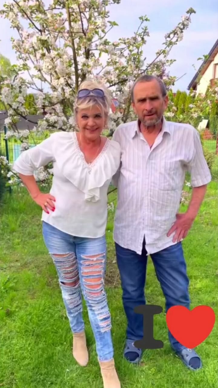 Elżbieta Czabator i Piotr Hubert Langfort w białych koszulach i jeansach, stoją objęci w sadzie