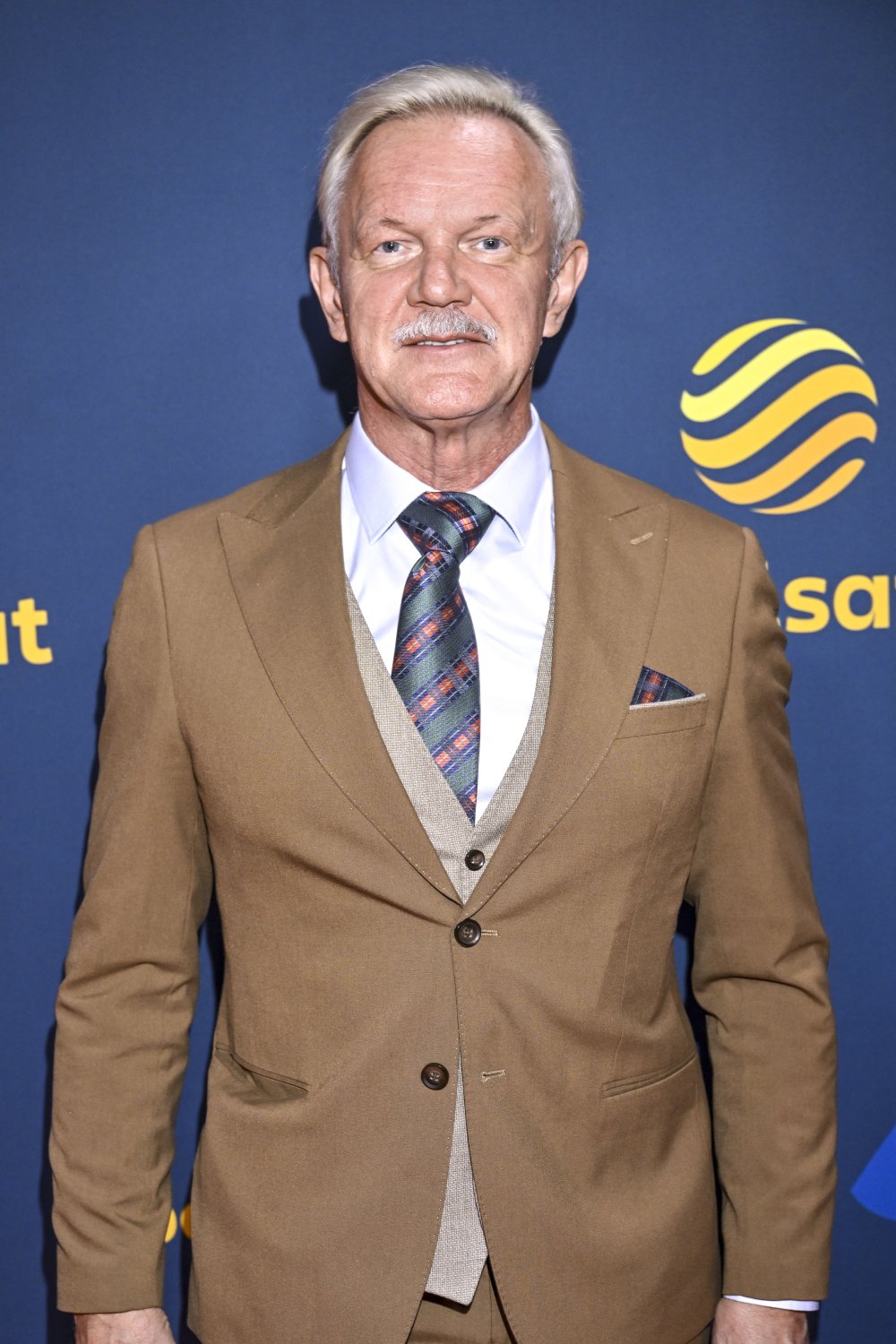 Cezary Pazura w karmelowym garniturze z siwymi włosami i wąsami