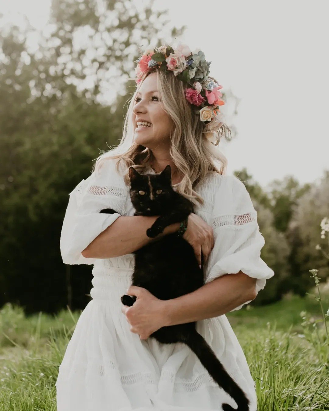 Katarzyna Bujakiewicz w wianku i białej sukience trzyma czarnego kota