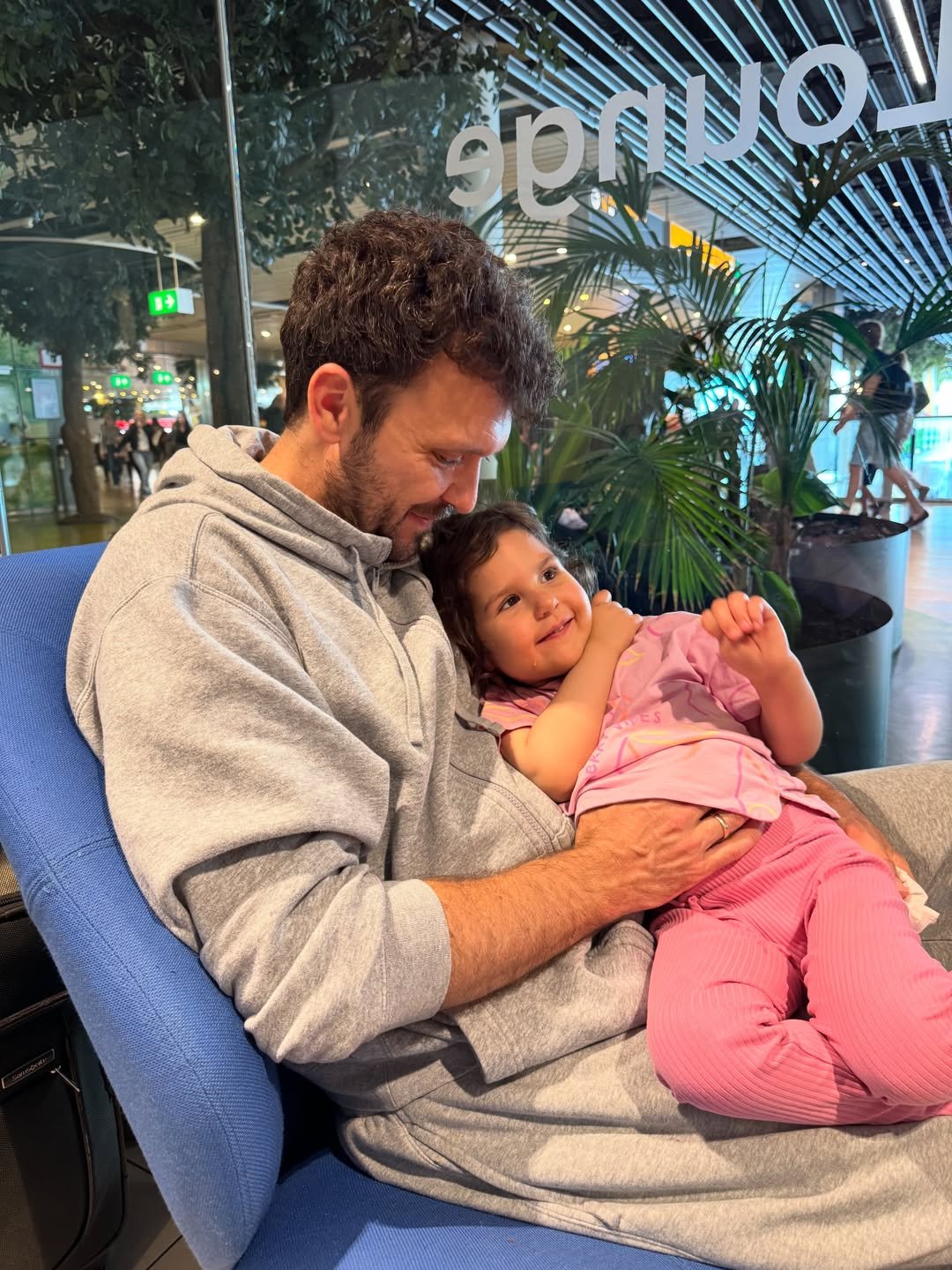 Bartek Marszałek w szarym dresie trzyma na kolanach ubraną na różowo córkę