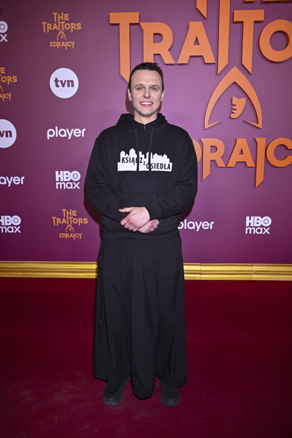 Rafał Główczyński w sutannie pozuje na ściance The Traitors. Zdrajcy