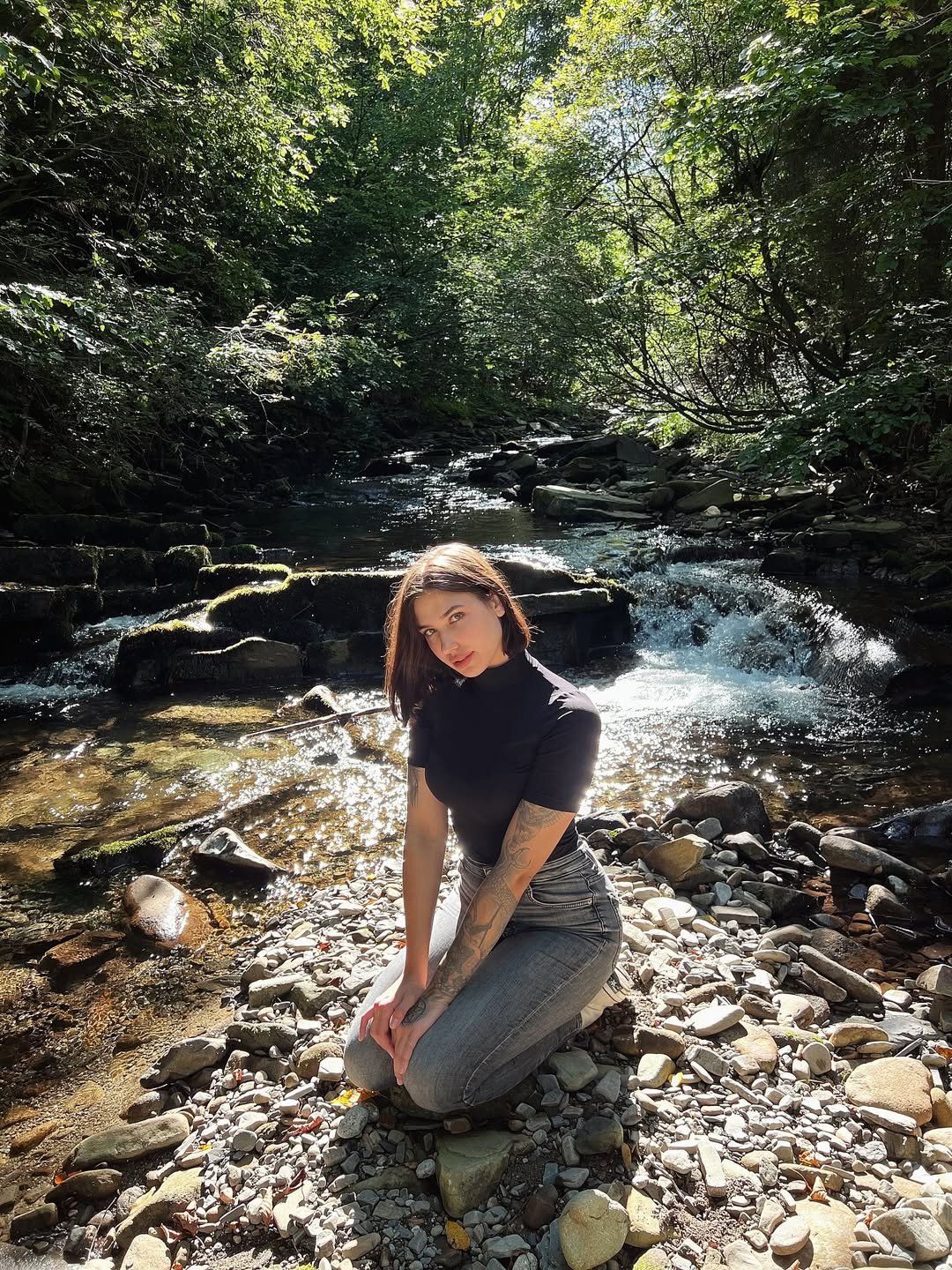 Złotanna siedzy przy strumyku w czarnym T-shircie i szarych jeansach