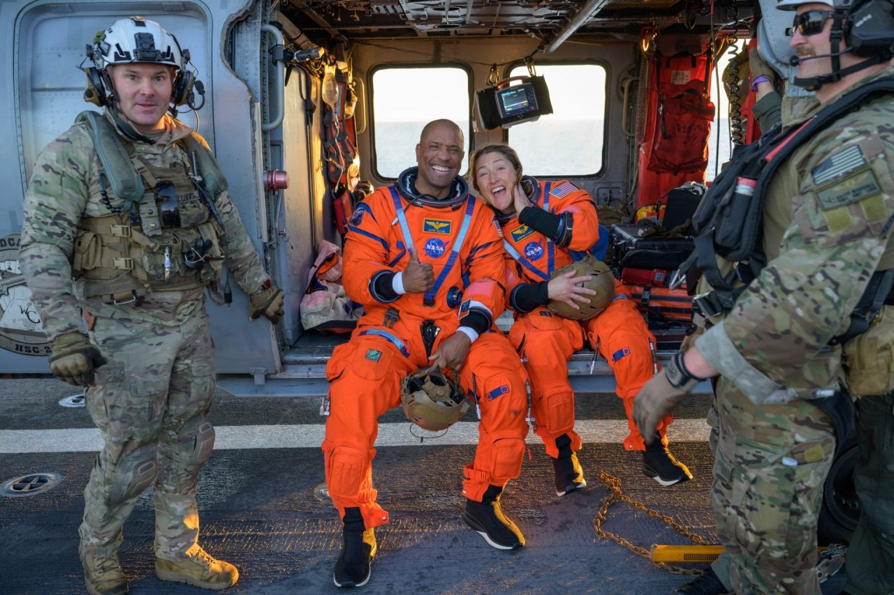 NASA astronaut Victor Glover, Artemis II pilot, left, and NASA astronaut Christina Koch, Artemis II mission specialist are seen sitting on a Navy MH-60 Seahawk from Helicopter Sea Combat Squadron (HSC) 23 on the flight deck of USS John P. Murtha after they and fellow crewmates CSA (Canadian Space Agency) astronaut Jeremy Hansen, Artemis II mission specialist, and NASA astronaut Reid Wiseman, Artemis II commander, were extracted from their Orion spacecraft after splashdown, Friday, April 10, 2026, in the Pac