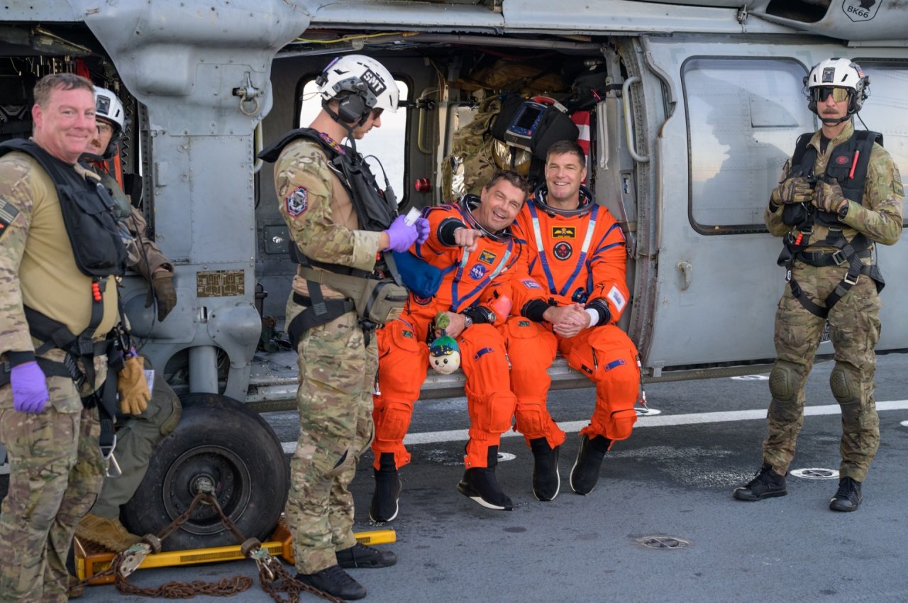 NASA astronaut Reid Wiseman, Artemis II commander, left, and CSA (Canadian Space Agency) astronaut Jeremy Hansen, Artemis II mission specialist, are seen sitting on a Navy MH-60 Seahawk from Helicopter Sea Combat Squadron (HSC) 23 on the flight deck of USS John P. Murtha after they and fellow crewmates NASA astronaut Christina Koch, Artemis II mission specialist, and NASA astronaut Victor Glover, Artemis II pilot, were extracted from their Orion spacecraft after splashdown, Friday, April 10, 2026, in the Pa