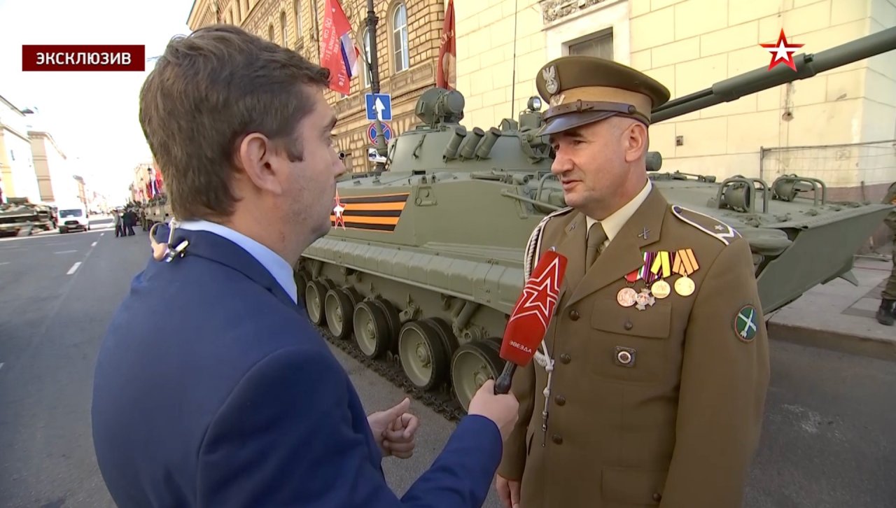 Jerzy Tyc w czasie wywiadu na tle czołgu