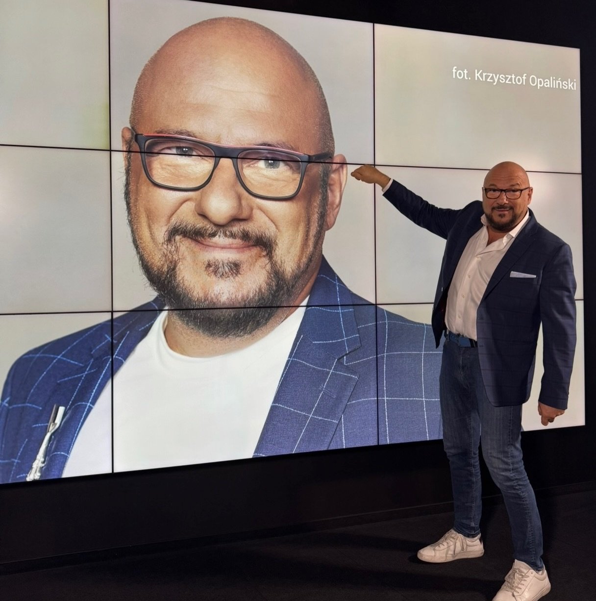 Piotr Gąsowski na tle wielkiego ekranu ze swoim zdjęciem