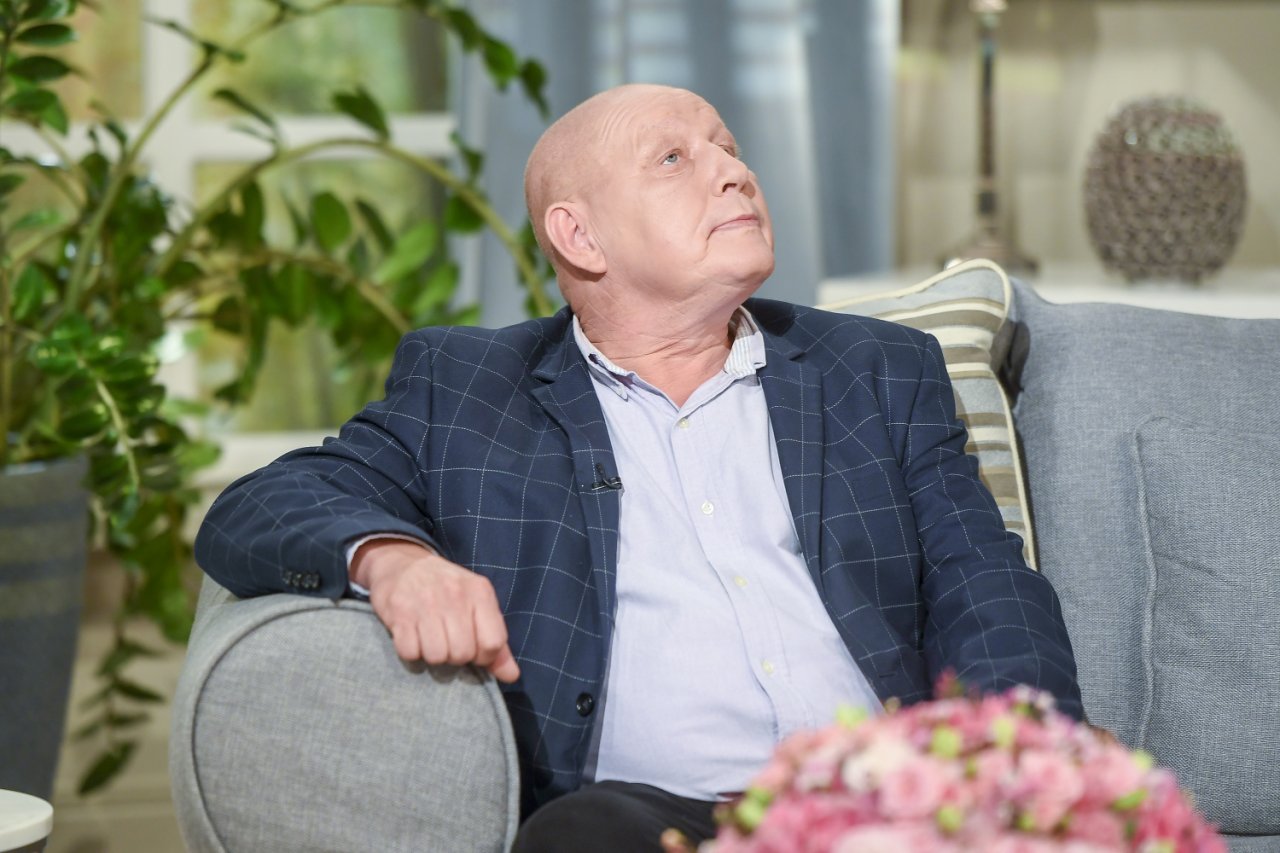 krzysztof jackowskii w jasnej koszuli i granatowej marynarce siedzi na szarej kanapie i patrzy na sufit