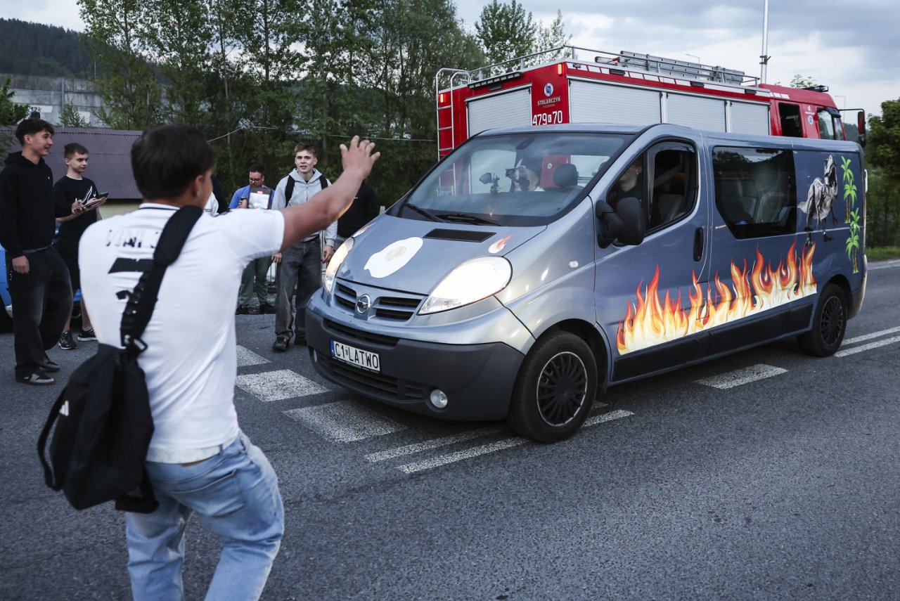 samochód typu bus z płomieniami na karoserii, w tle samochód strażacki, na pierwszym planie młody mężczyzna robiący zdjęcie