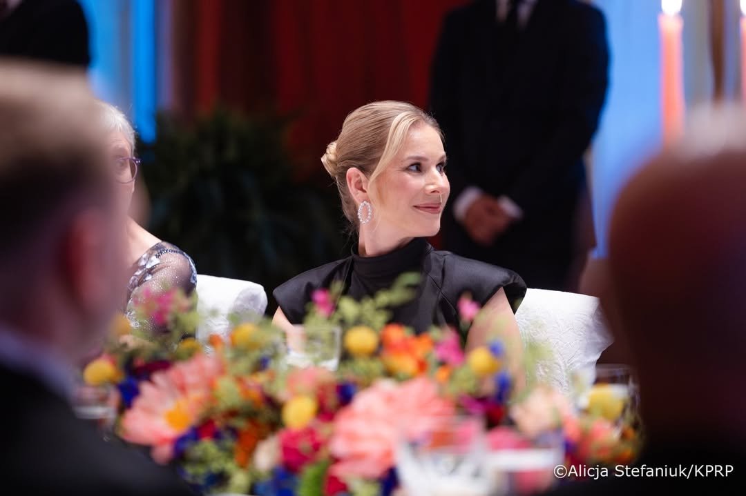 Marta Nawrocka siedzi przy stole zakryta kwiatami