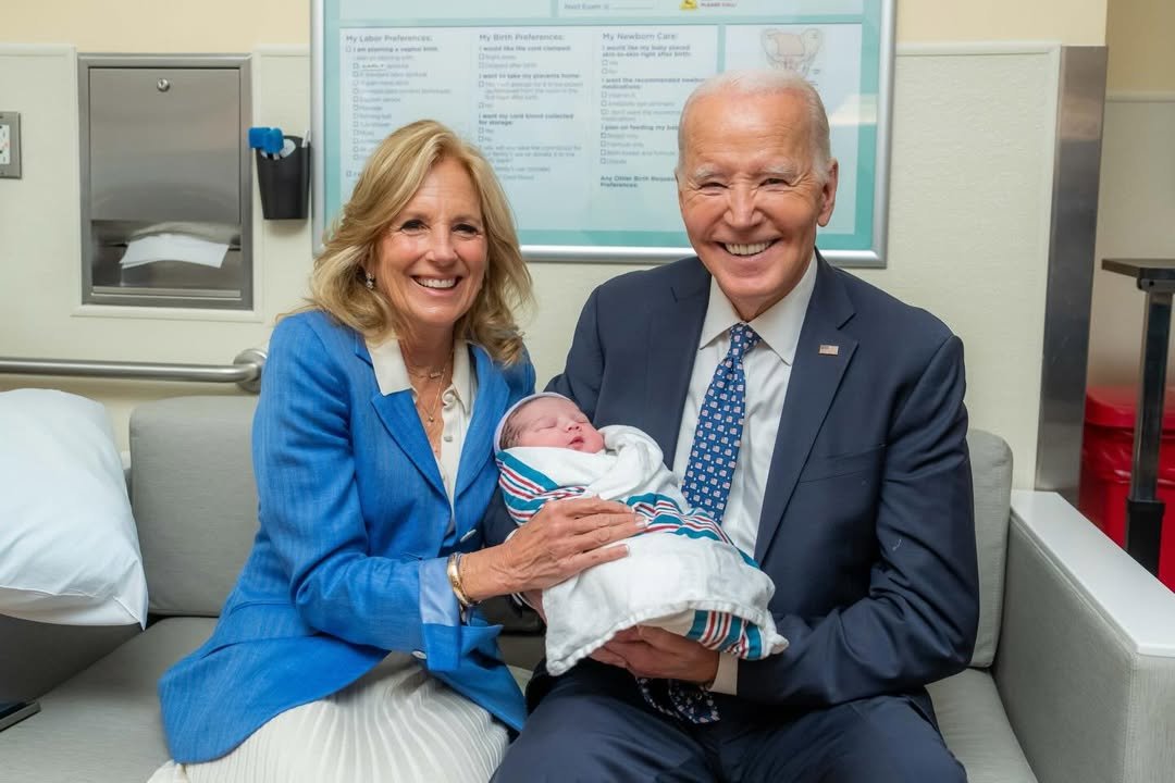 joe i jill bidenowie siedzą obok siebie i trzymajją noworodka w ramionach