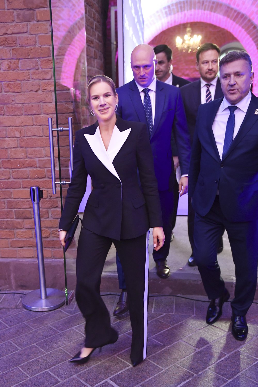 Marta Nawrocka w czarno-białym komplecie idzie w towarzystwie kilku mężczyzn