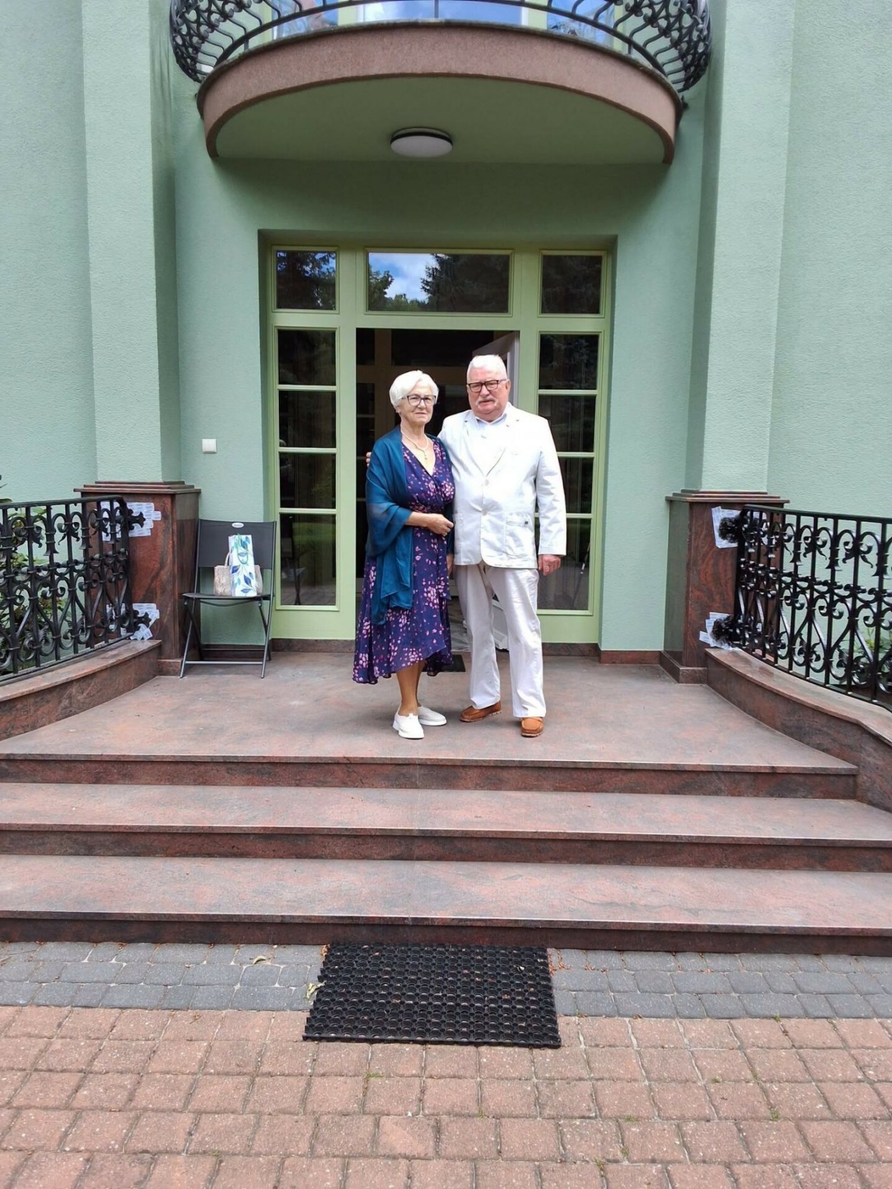 lech wałęsa z żoną stoi na tarasie pod okazałym budynkiem