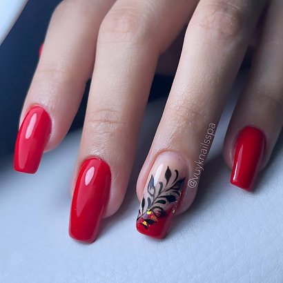 Czerwony manicure na kwadratowym kształcie z czarnym zdobieniem w postaci liścia.
