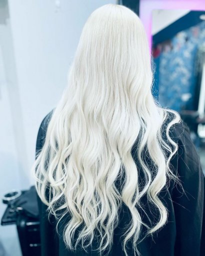 Długie, cieniowane i falowane włosy w jednolitej koloryzacji platynowy blond.